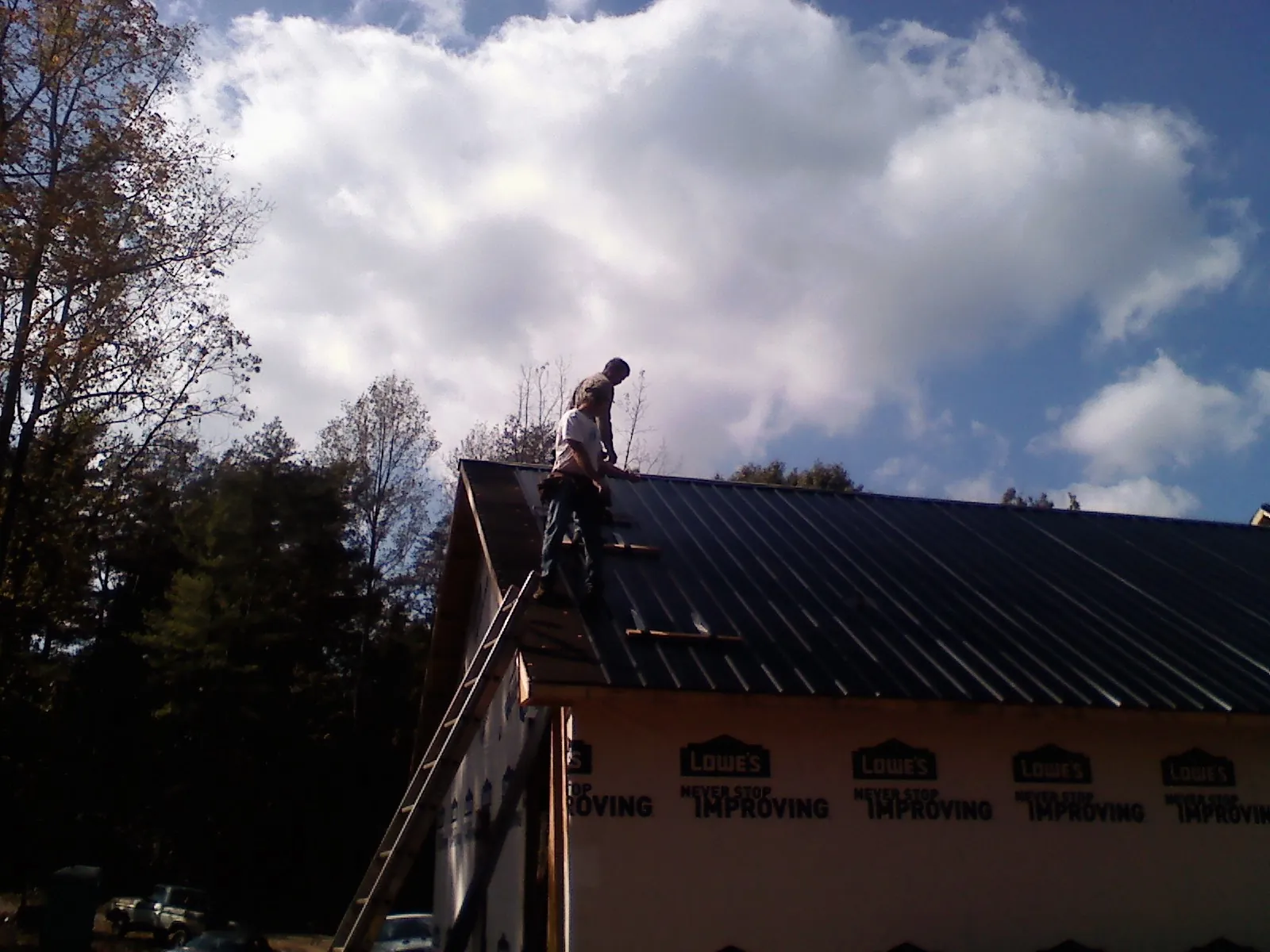 Roofer fastening dark metal panels high against a cloudy sky, from a Roof Inspection job in Santee