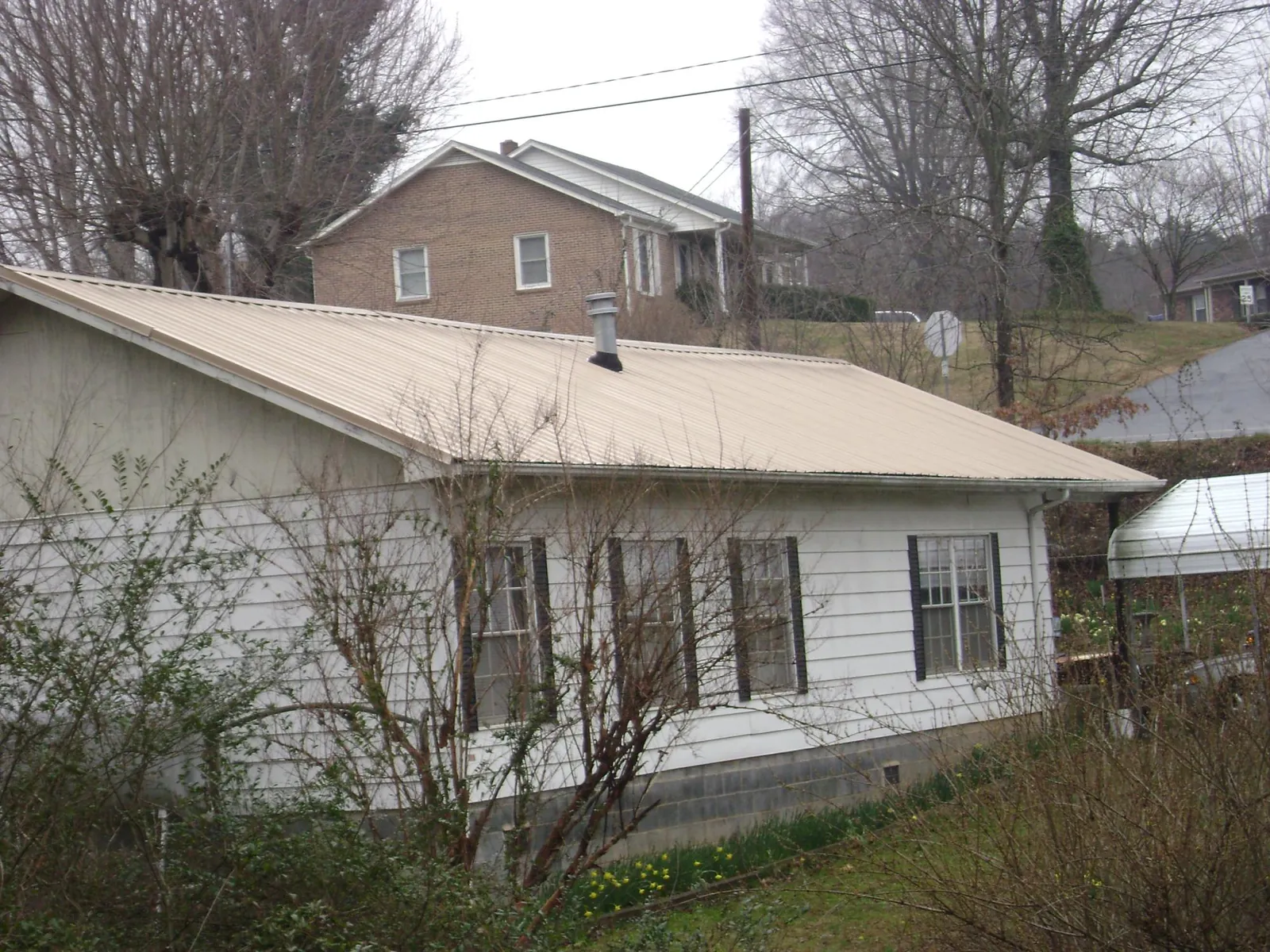 Tan metal roof on a white sided house set into a hillside — Commercial Roofing by Roofing Brothers in Santee